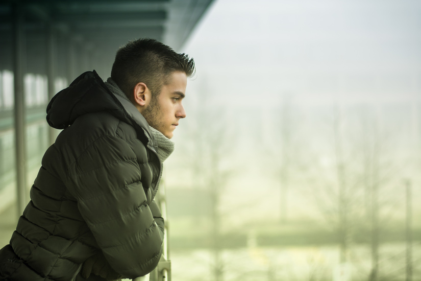 young man standing on balcony during winter looking sad - seasonal affective disorder