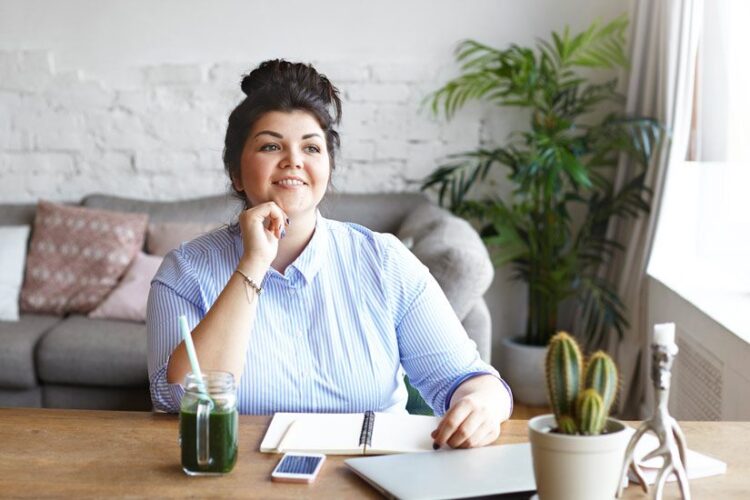 pretty brunette young woman sitting at coffee table at home smiling and making notes - languishing