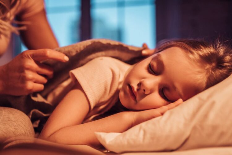 cropped shot of mom tucking her little girl into bed - bed time routine