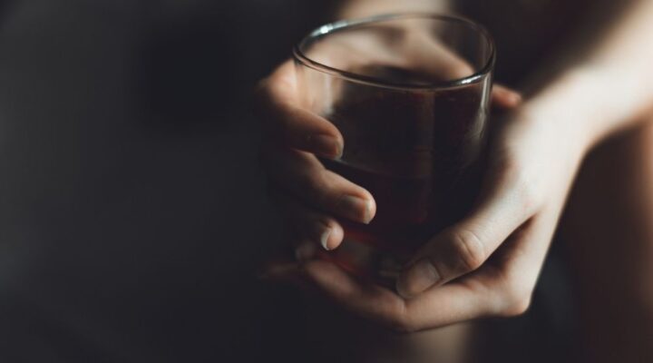 Close-up of a person's hands gently holding a glass of dark liquid,