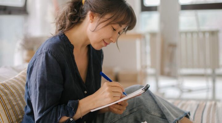 Woman sitting comfortably indoors, smiling as she writes in a notebook
