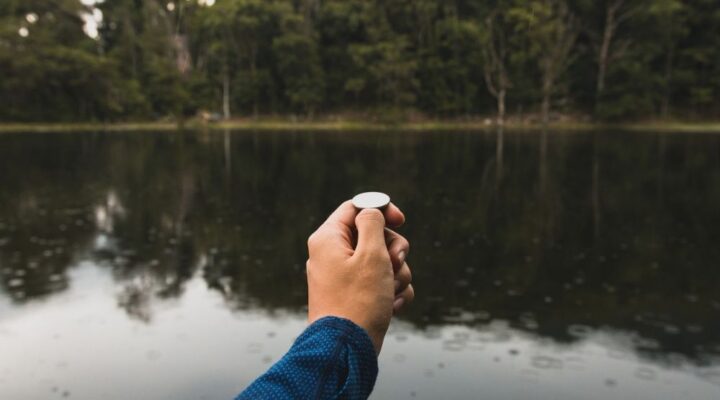 Close-Up Of Hand Holding Coin, water in background with trees