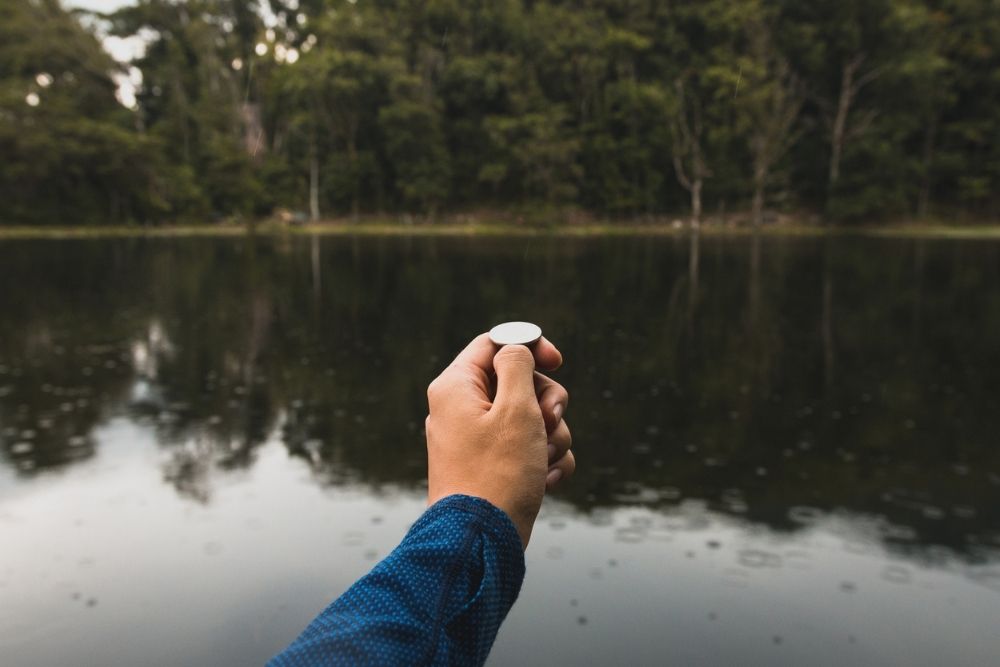 Close-Up Of Hand Holding Coin, water in background with trees