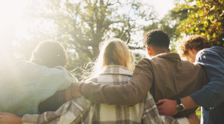 A group of people stand close together outdoors with their arms around each other, symbolizing support and community.