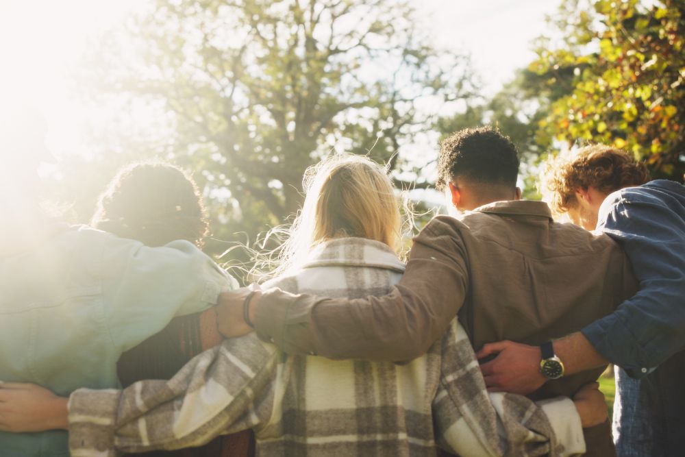 A group of people stand close together outdoors with their arms around each other, symbolizing support and community.